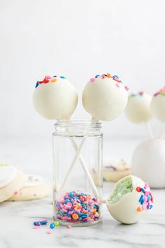 white cake pops with sprinkles in a glass jar on a marble counter