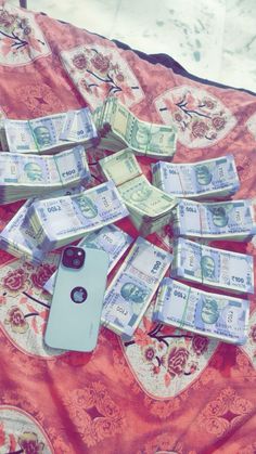 a pile of money sitting on top of a bed next to a cell phone in the middle