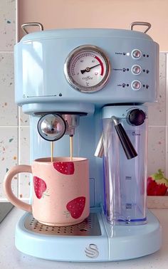 a blue coffee maker sitting on top of a counter next to a cup with liquid in it