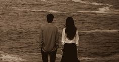 two people standing on the beach looking out at the water