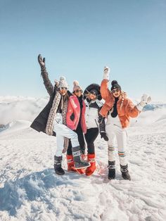 three women standing on top of a snow covered slope with their arms in the air