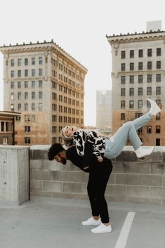 a man and woman standing on top of a roof next to each other with buildings in the background