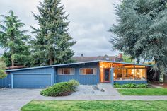 a blue house with trees and grass in the front yard on a cloudy day at dusk