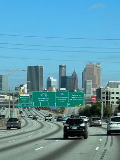 cars driving down the highway in front of large city buildings and tall skyscrapers on a clear day