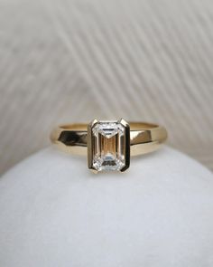 a gold ring with an emerald cut diamond in the center on a white cloth background