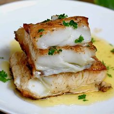 two pieces of fish sitting on top of a white plate covered in sauce and parsley