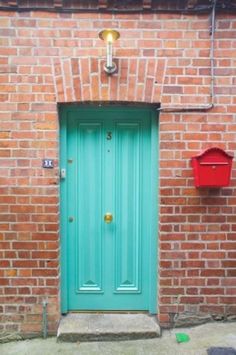 a brick building with a green door and two red boxes on the wall next to it