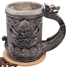 a metal mug with a dragon handle and some coffee beans on the table next to it