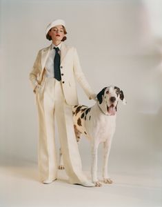 a woman standing next to a dog wearing a white suit and tie with her hands in her pockets