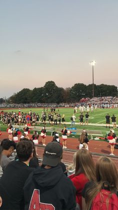 a group of people standing on top of a field next to a football field with cheerleaders