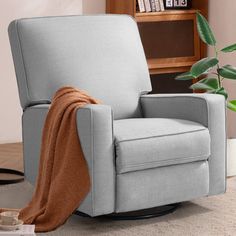 a chair with a blanket on it next to a book shelf and potted plant