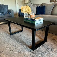 a coffee table with books and flowers on it in front of a gray couches