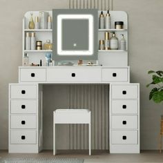 a white vanity with drawers and a mirror on it's wall next to a potted plant