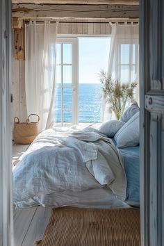 a bedroom with an ocean view is shown through the open door to another room that has white curtains and blue bedding