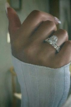 a woman's hand with a diamond ring on top of her finger, in front of a mirror