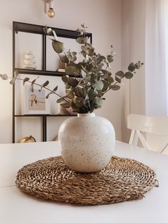 a white vase sitting on top of a table next to a wicker place mat