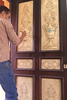 a man is painting the side of a wooden door with decorative glass panels on it