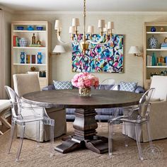 a dining room table surrounded by chairs and bookshelves with paintings on the wall