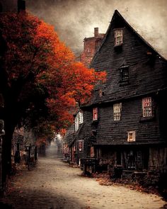 an old black house with red leaves on the trees in front and dark clouds above it