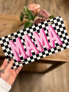 a person holding up a sign with the word mam in pink and black checkerboard