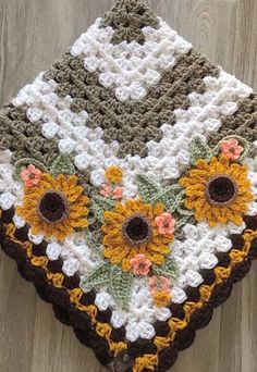 a crocheted dishcloth with sunflowers and leaves on the bottom, sitting on a wood floor