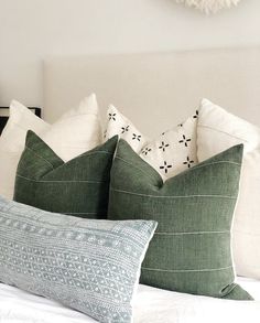 two green pillows sitting on top of a white bed next to a wall mounted clock