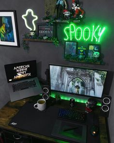 a desk with a laptop, keyboard and monitor lit up by neon signs on the wall