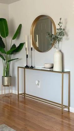 a living room with a mirror, vases and plants on the side table in front of it