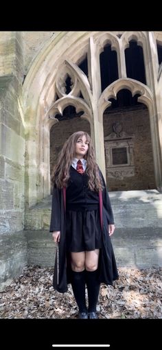 a woman in a black dress and red tie is standing outside an old building with leaves on the ground