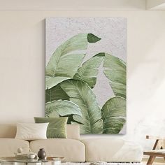 a living room with a white couch and large green leaf painting on the wall above it