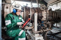 a woman in green and white uniform working on an industrial machine with headphones around her ears