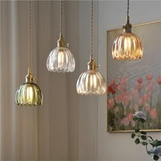 three glass pendant lights hanging from a ceiling in a room with flowers on the wall