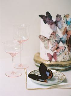 a cake with butterflies on it next to two wine glasses