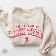 "💅 Stay cozy and stylish this Valentine's Day with our \"Cupid's Favorite Nail Tech\" Sweatshirt--a must-have for nail enthusiasts. Elevate your wardrobe and showcase your expertise with this comfortable and chic pullover, embodying the spirit of Cupid's favorite nail technician. 💅 SPECS: * UNISEX heavy blend crewneck sweatshirt (blissfully comfy); please refer to size chart in listing photos for more details * Air jet yarn for softer feel and reduced pilling * Pre-shrunk 50% cotton, 50% polyester  * Loose fit * Runs true to size * Double-needle stitched collar, shoulders, armholes, cuffs and waistband 💅 DTG PRINTING (Direct to Garment): How does it work? * With DTG printing, a printer directly applies the ink onto the t-shirt/sweatshirt with inkjet technology. It's sort of like printin Valentines Nail, Tech Gift, Tech Shirt, Nail Technician, Tech Gifts, Valentines Nails, Nail Tech, Crewneck Sweatshirt, Clothing Brand