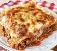 a white plate topped with lasagna covered in cheese and sauce on top of a checkered table cloth