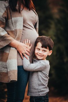 a pregnant woman holding her son's hand while he stands next to his belly