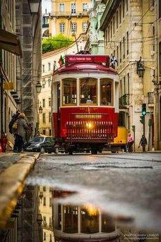 a red trolley car traveling down a street next to tall buildings