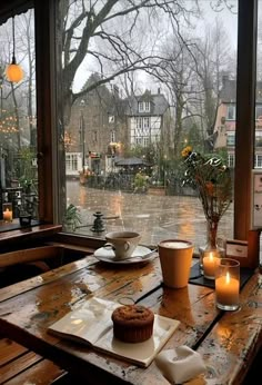 a wooden table topped with a muffin next to a window covered in raindrops