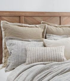 a bed topped with lots of pillows next to a wooden headboard