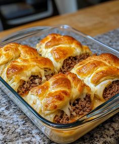 a glass casserole dish filled with meat and cheese covered pastries on top of a granite counter