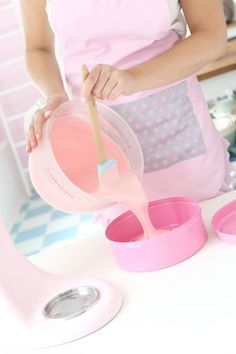 a woman in an apron is pouring pink liquid into a bowl with a wooden spoon