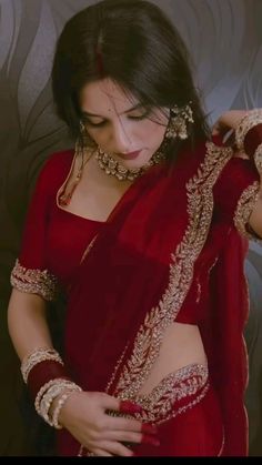 a woman in a red sari and jewelry is holding her hand on her hip