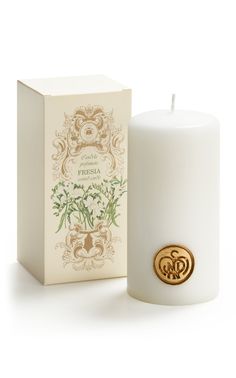 a white candle next to a box on a white surface with a gold emblem in the middle