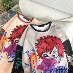 two sweatshirts with anime characters on them sitting next to each other in front of a bed