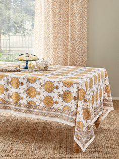 a table covered with a yellow and white tablecloth in front of a large window