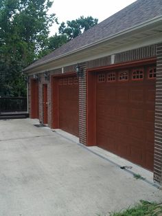 two brown garage doors are open in front of a brick building with a black fence