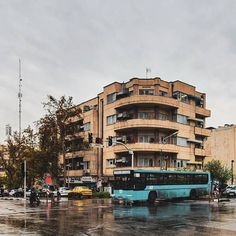 a blue bus parked in front of a tall building on a rainy day with cars driving by