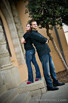 a man and woman standing next to each other in front of a tree with their arms around each other