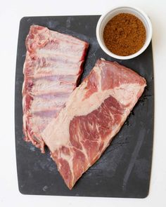 two pieces of meat sitting on top of a cutting board next to a bowl of seasoning