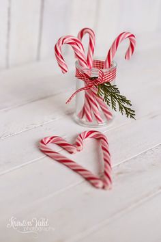 two candy canes in a glass vase on a white wooden table with a heart shaped decoration